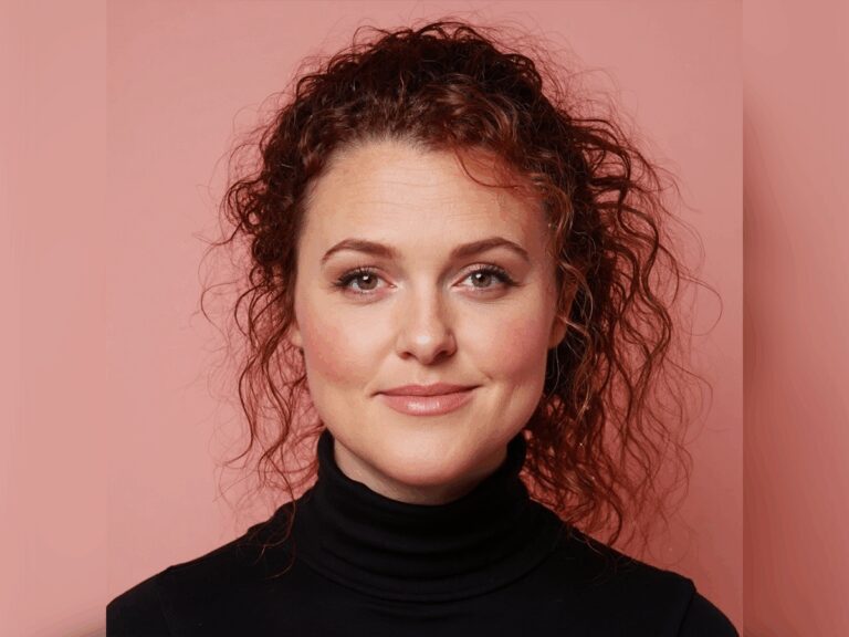 Talent agent Brandi England smiling in a black turtleneck shirt in front of a pink background.