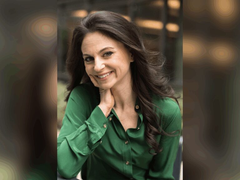 Casting director Danielle Pretsfelder Demchick smiling outside in a green long sleeved button down shirt with her hand on her cheek.