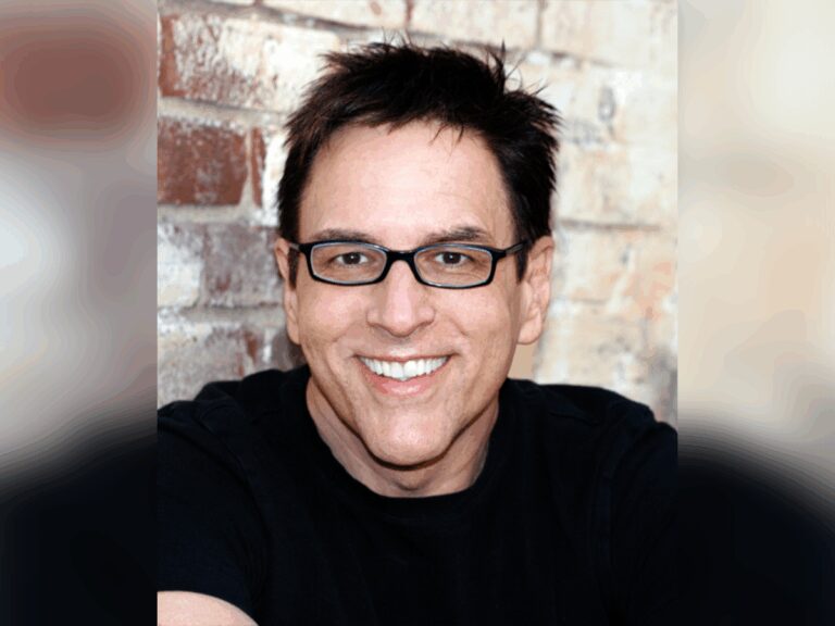 Casting director Robert J. Ulrich smiling in a black sweater in front of a brick wall.