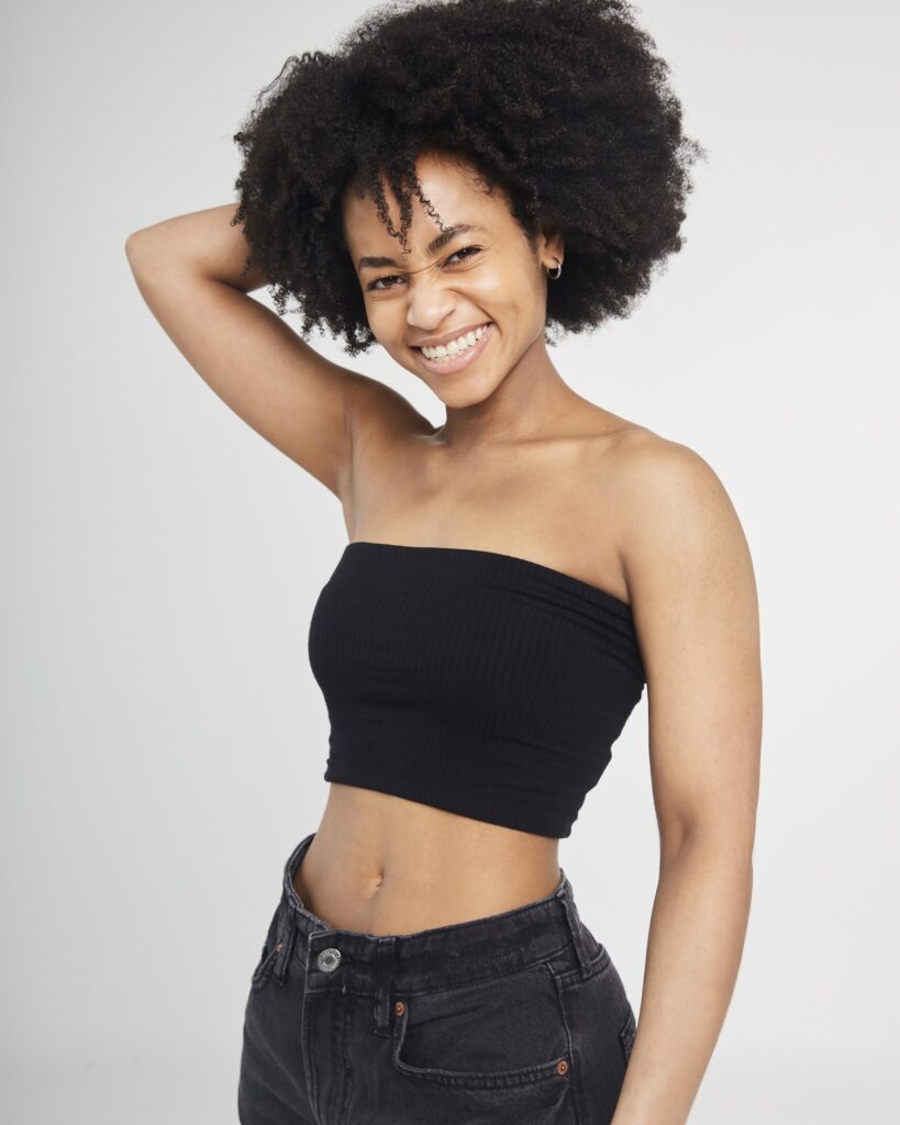 Sarah Murray smiling with her arm behind her head in black jeans and a black crop top.