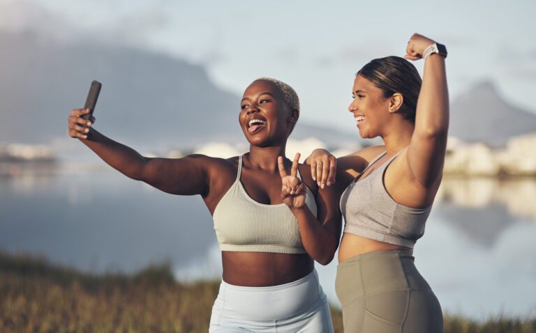 Two women of color taking a selfie outdoors before going for a run together.