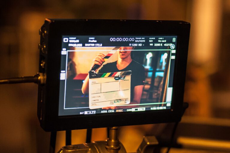 Man holding a clapper board in front of a rolling camera on a film set.