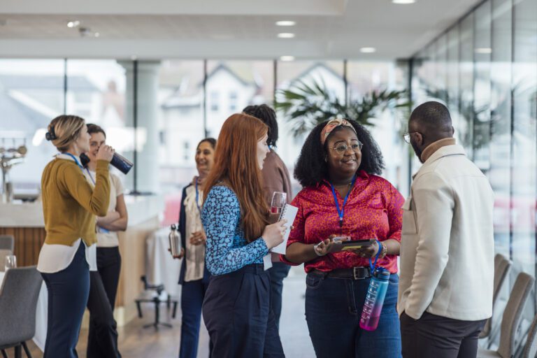 Diverse group of women and one man networking and chatting in an event space.