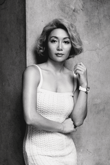 Black and white filter of Juju Chan Szeto in a white dress with her arm on her fist pointing up.