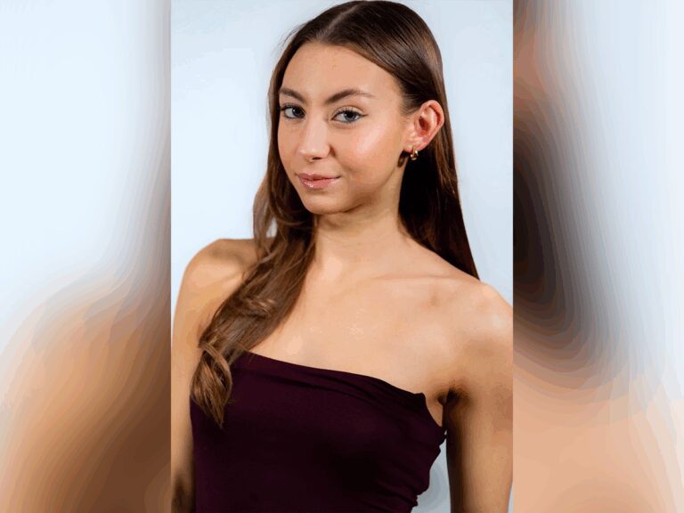 Brooke Vass smiling in front of a gray backdrop in a burgundy top.