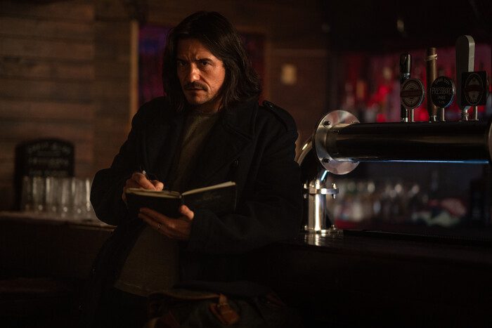 Long-haired Orlando Bloom in a dimly lit pub reading a book.