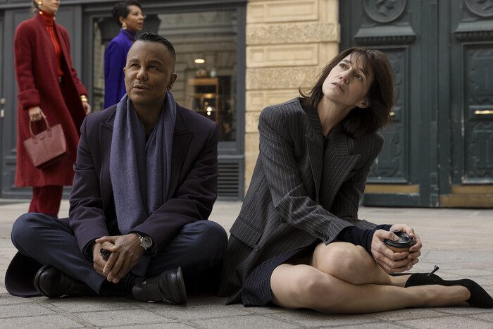 Two people sitting on the floor in suits outside in the street on the curb.