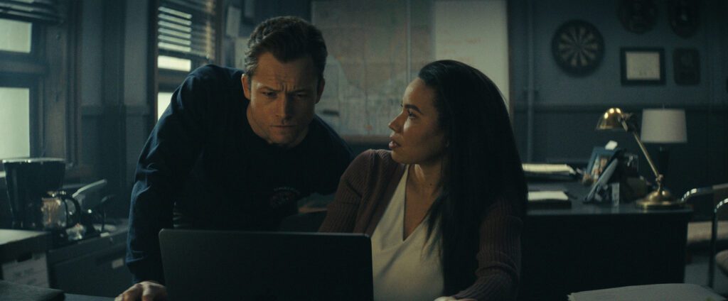 Taron Egerton and Jurnee Smollett chatting in a dimly lit office.
