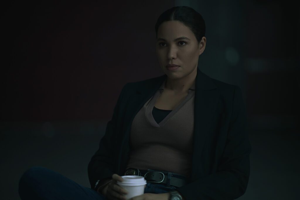 Jurnee Smollett sitting at her desk in a brown shirt and blazer with a coffee in hand.
