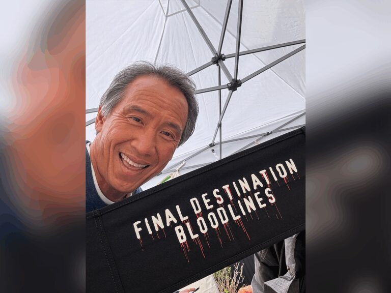 Tinpo Lee smiling in a tent on set next to a director chair with the Final Destination: Bloodlines logo.