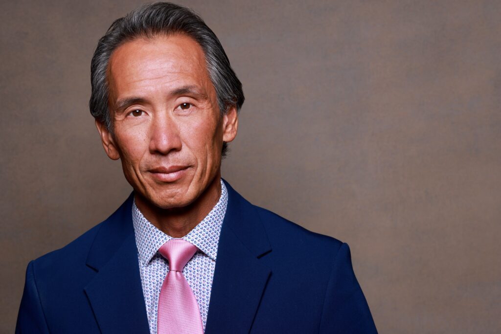 Actor Tinpo Lee smiling in a blue suit with a pink tie.