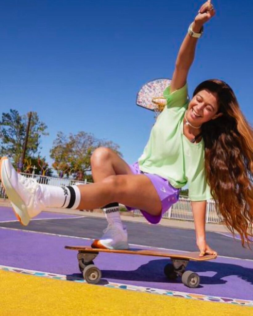 Pauline Sala on a skateboard, leg kicked out and arm in the air at a skatepark.