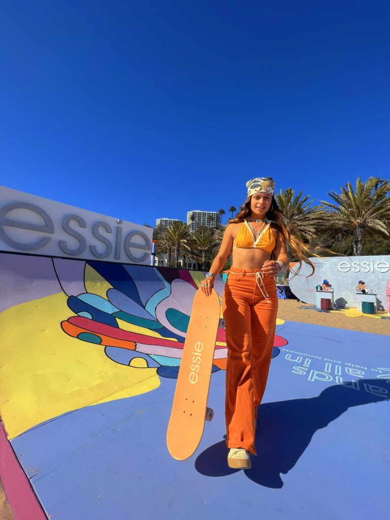 Pauline Sala at the Venice Beach skatepark with a board in hand in 70s style clothing.