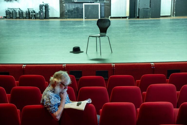 Actor sitting in an empty theater researching his character. A chair and hat are on am otherwise bare stage.