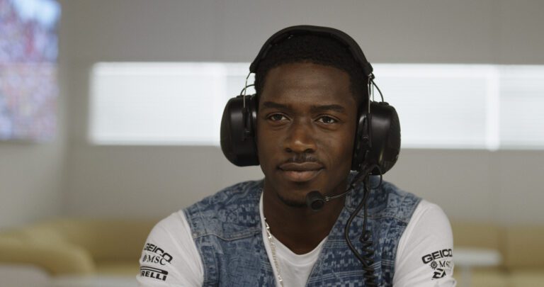 Damson Idris talking in a commentary booth with headphones on in a denim jacket.