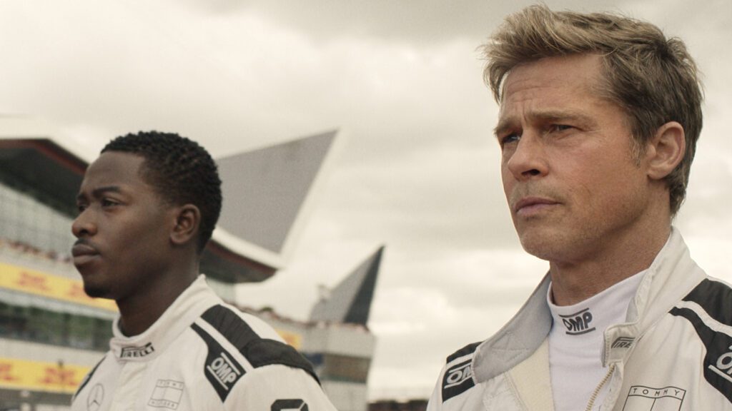 Pitt in black and white Formula One racing driver uniforms walking to the track outside.