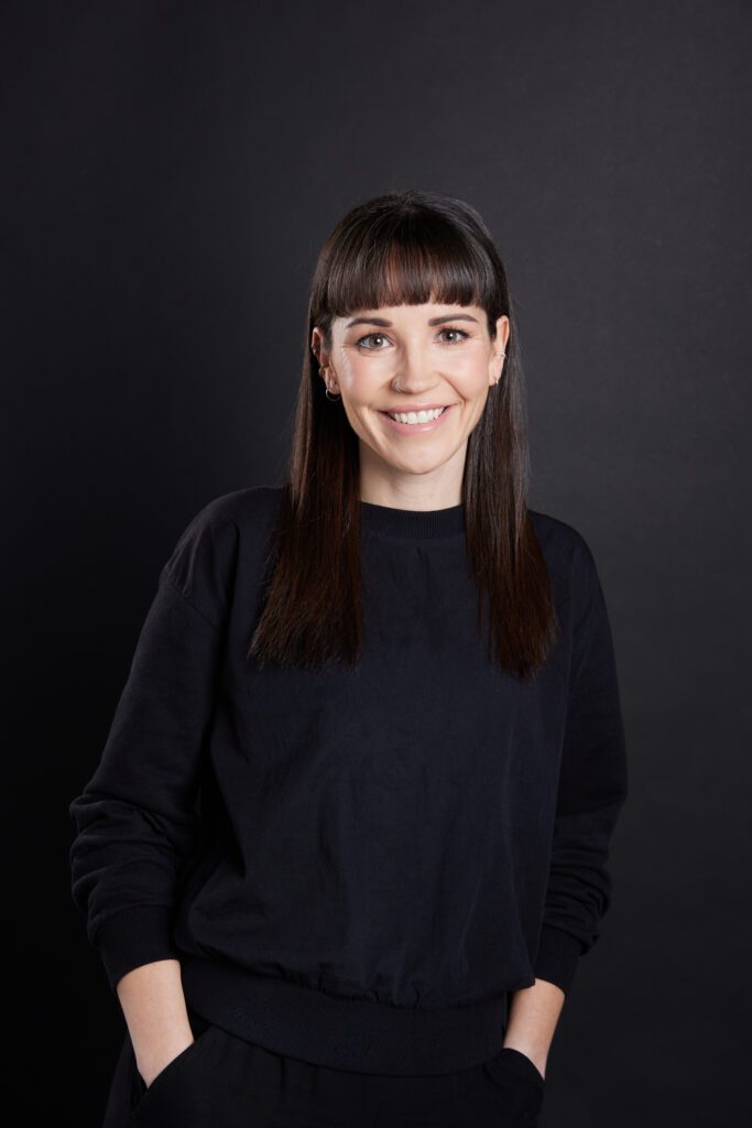 Kello Inclusive founder Katie MacMillan smiling in a black long sleeve outfit, hands in her pockets.
