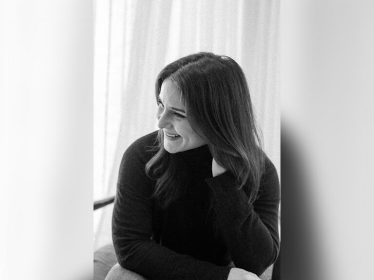 Casting director Rebecca Dealy in a black sweater sitting down and smiling. A black and white filter is applied.