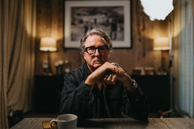 Casting director John Papsidera sitting at his desk, dressed in black with his hands folded in front of him.