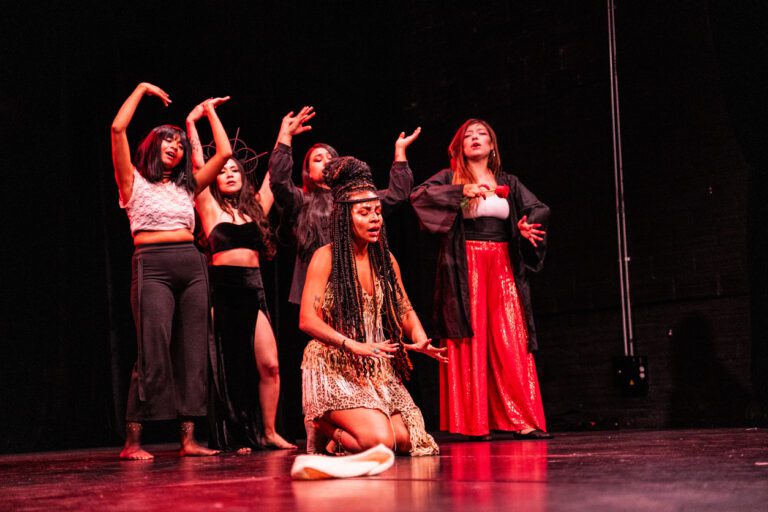 diverse cast of actresses performing a musical onstage in African, Spanish and modern outfits.