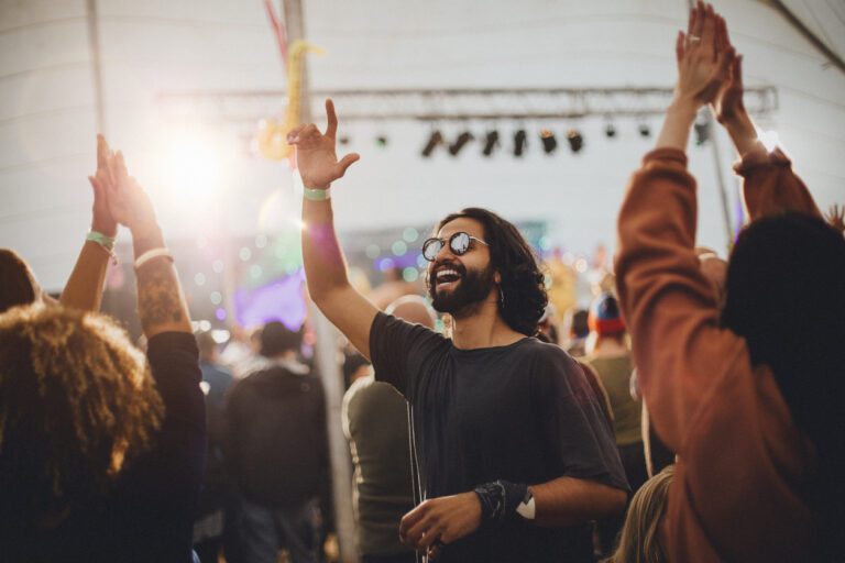People at a music festival hanging out and dancing. A long-haired bearded man with sunglasses is vibing to the music.