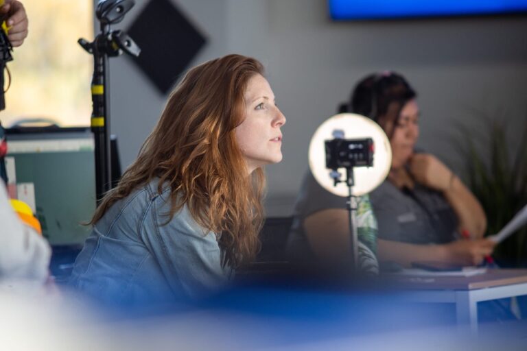 Casting Director Sarah Cayce on set in a denim jacket watching actors perform and audition.