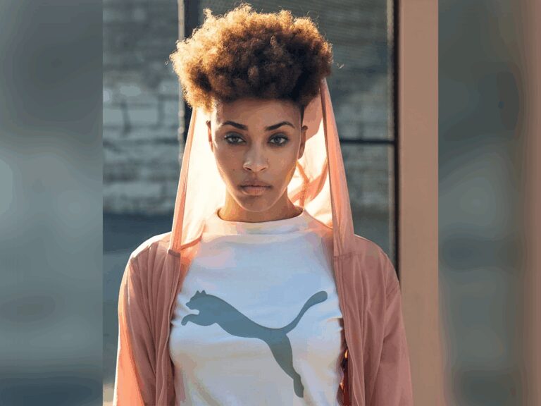 Model and actress Aconda Williams outside looking fierce in a pink hoodie and a white Puna shirt.