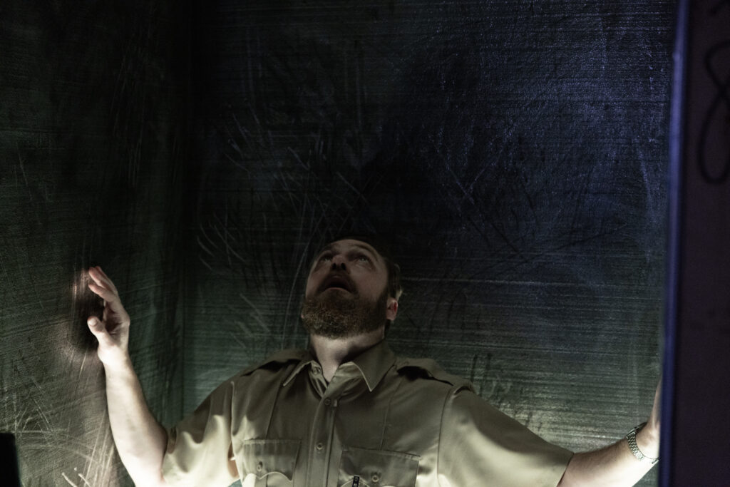 Ross Marquand terrified in an enclosed steel pod with scratch marks on the walls.