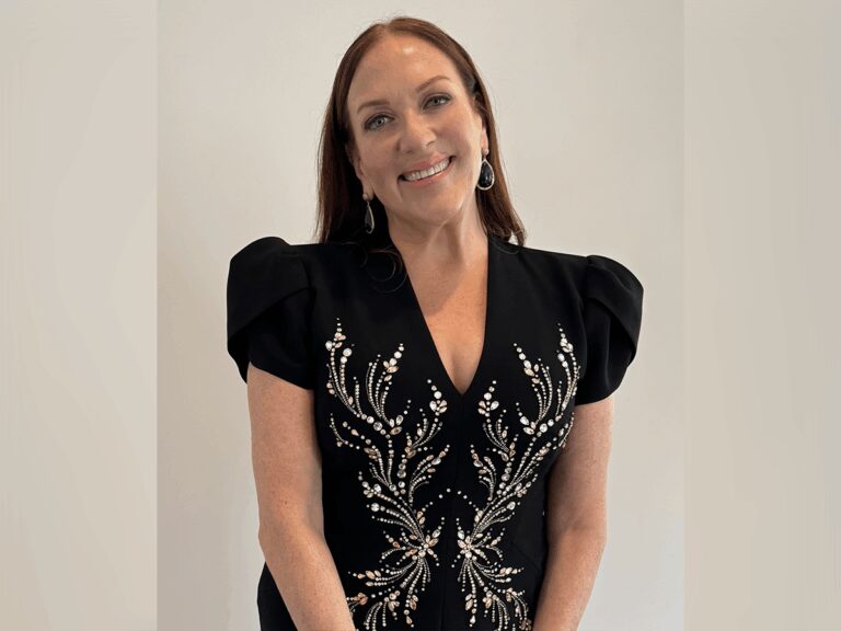 Severance casting director Rachel Tenner smiling indoors in a black blouse with a silver leaf pattern.