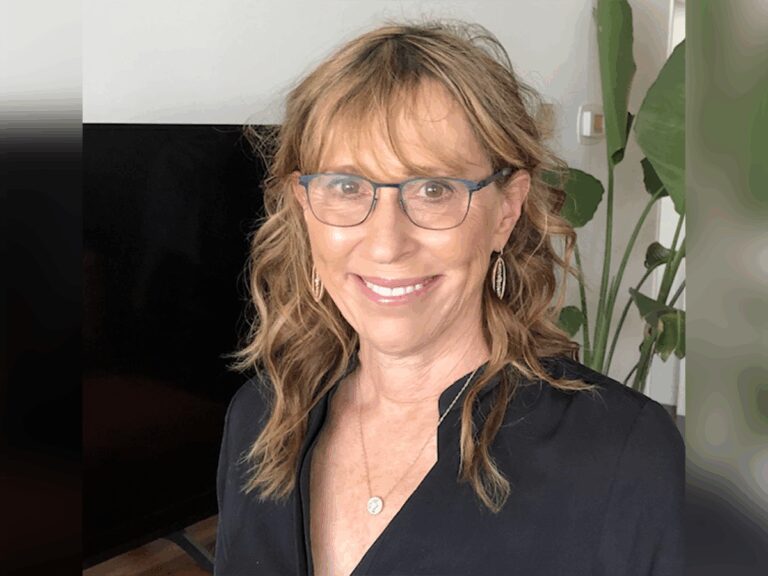 Casting director Sharon Bialy smiling in a black shirt in a living room near tall plants.