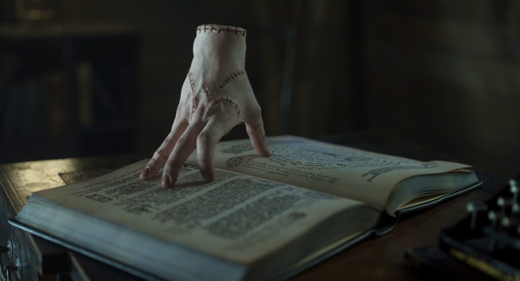 Thing from the Addams Family standing on an open book in a dark room.