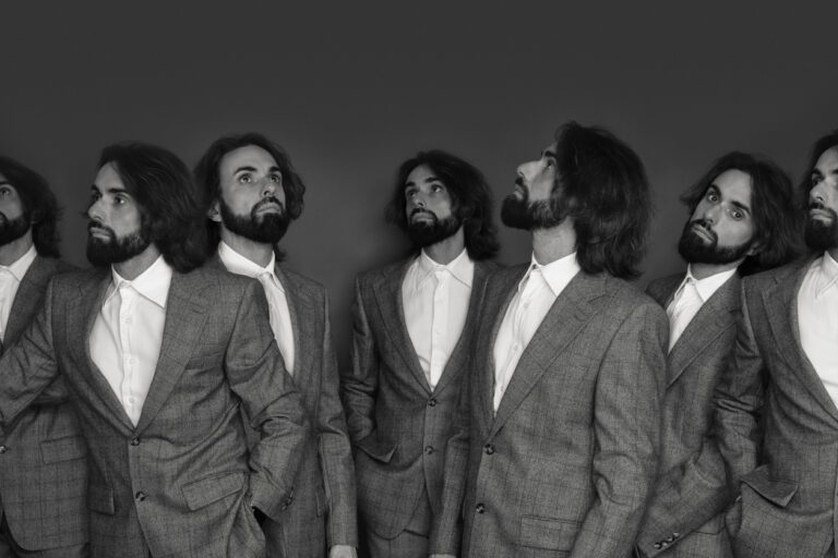 Long haired, bearded actor wearing a suit, surrounded by many clones. Filter is black and white.