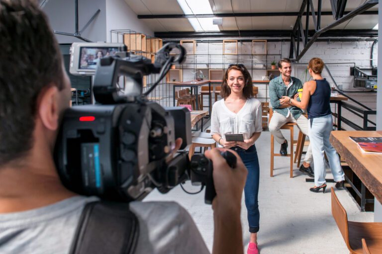 Female actress being filmed for a tv show in an empty office setting as two other actors work the background.
