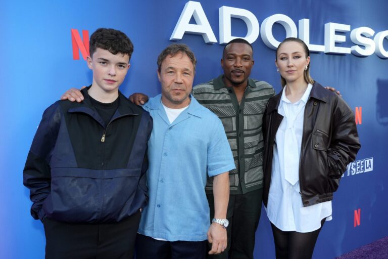 The cast of Netflix's Adolescence standing in front of a blue promotional poster.
