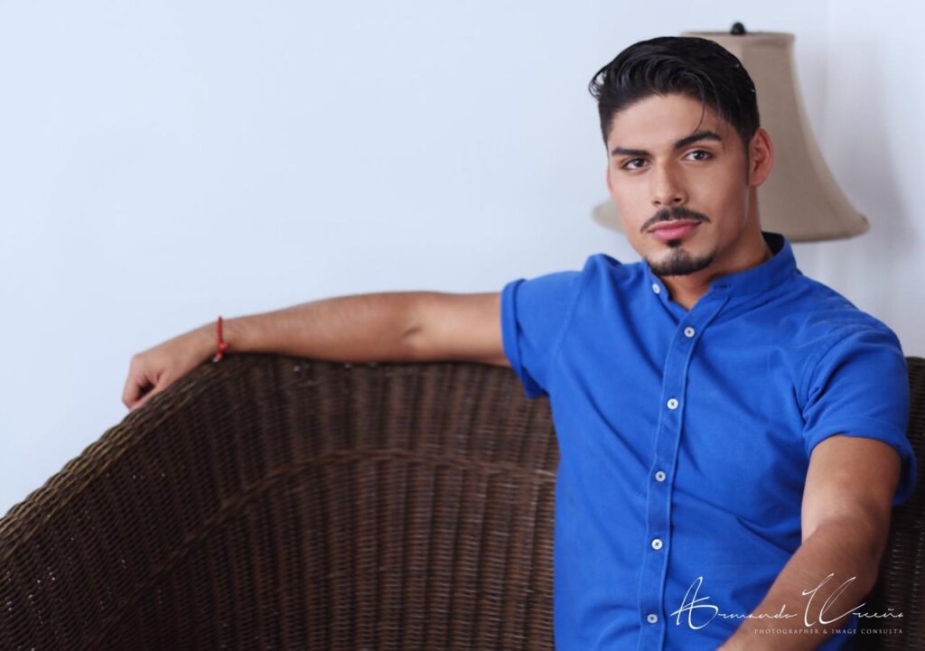 Actor Kerin Castillo in a nice blue shirt sitting asymmetrically on a brown couch.