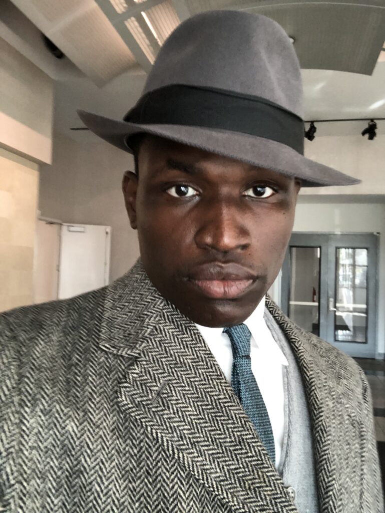 Justin Dinkins in a 1960s coat and hat on the set of The Marvelous Mrs. Maisel.