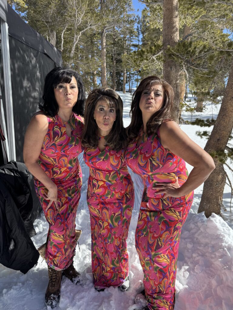 Stephanie Jones (right) and two other women dressed as 50's-era Spanish women wearing pink outfits outside in the snowy woods.